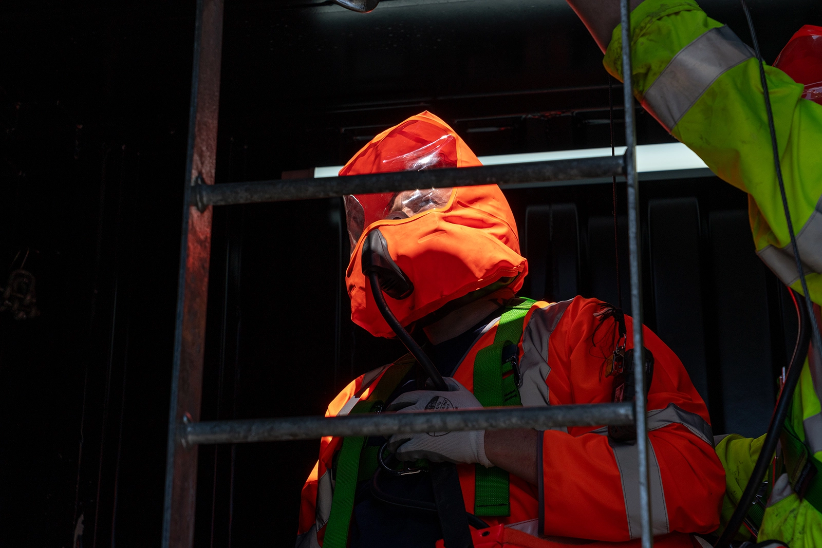 Low lighting shot of a person wearing bright orange hi-vis breathing apparatus and PPE in a Confined Space tank on a HSS Training course