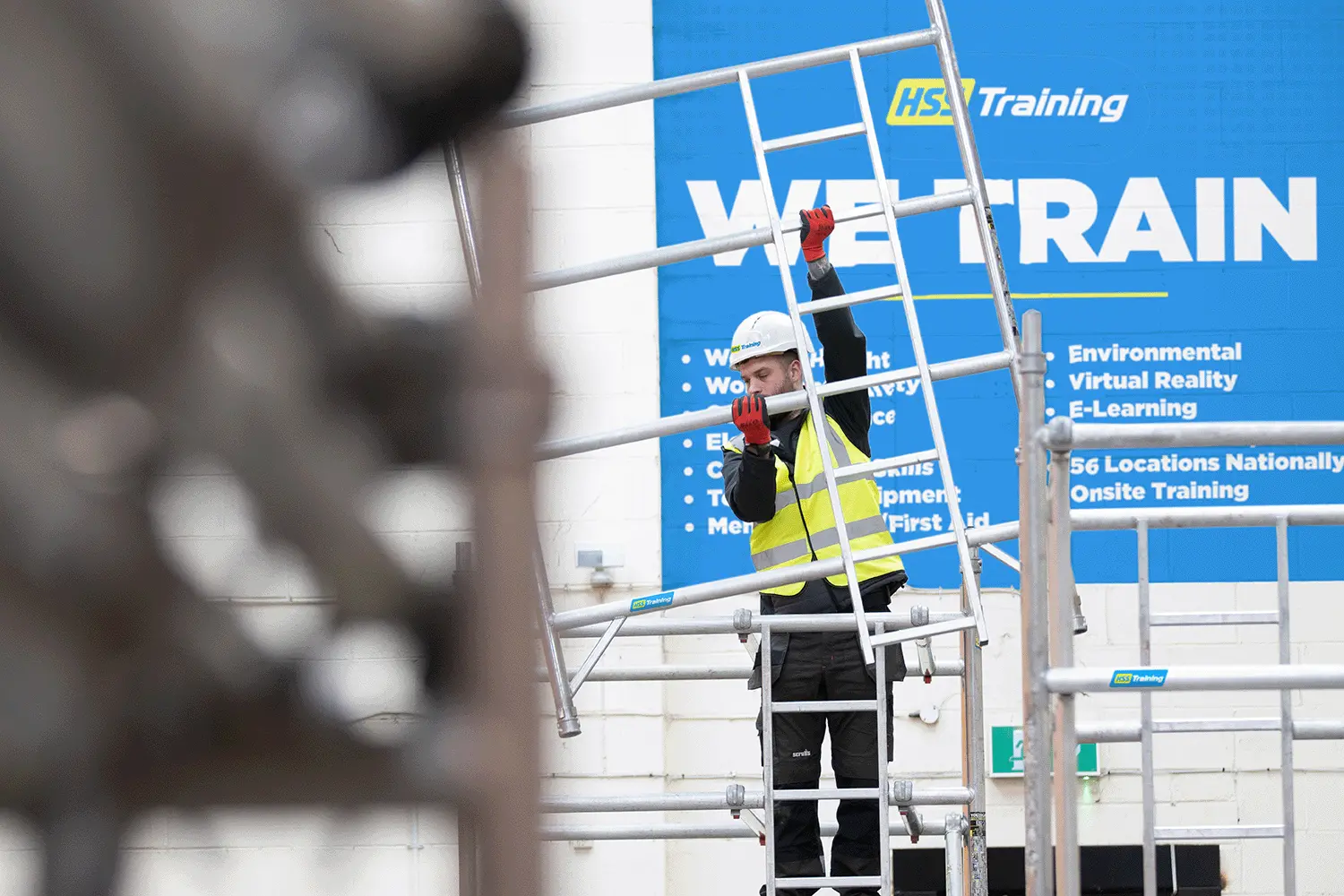 Man wearing hard hat and hi vis vest on a HSS Training PASMA Work at Height course learnign how to assemble a mobile access tower