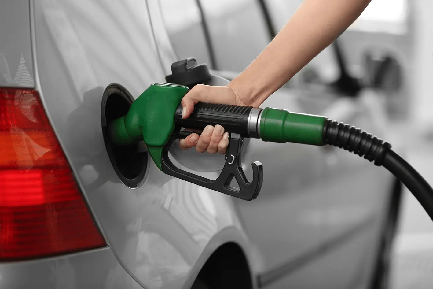 Closeup of a hand holding a petrol pump filling up a car on a forecourt