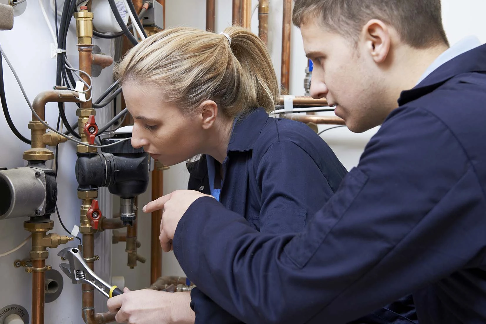 Two people in blue overalls working to fix some hot water pipework